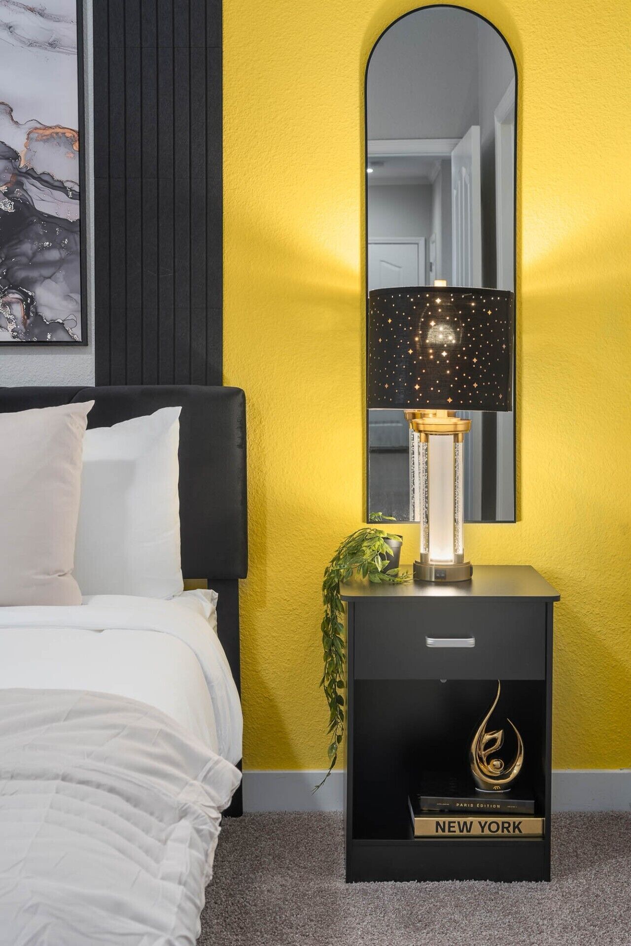 Ein Schlafzimmer mit einem Bett, einem Nachttisch mit Lampe, einem Spiegel und einem gerahmten Bild an der Wand.