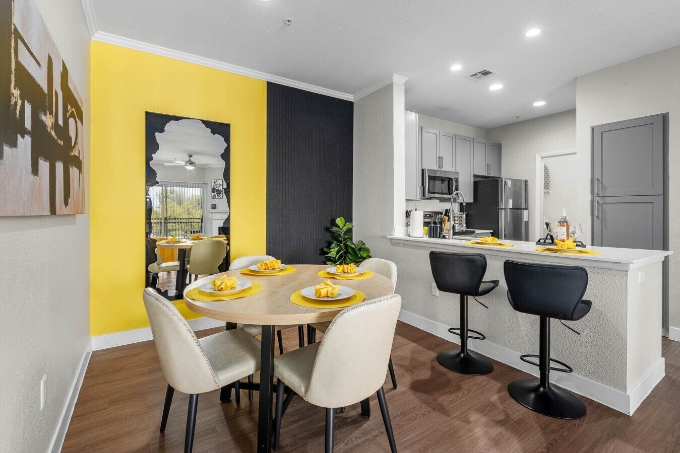 A modern kitchen with white cabinets, a central island, and a dining area with a round table and chairs.