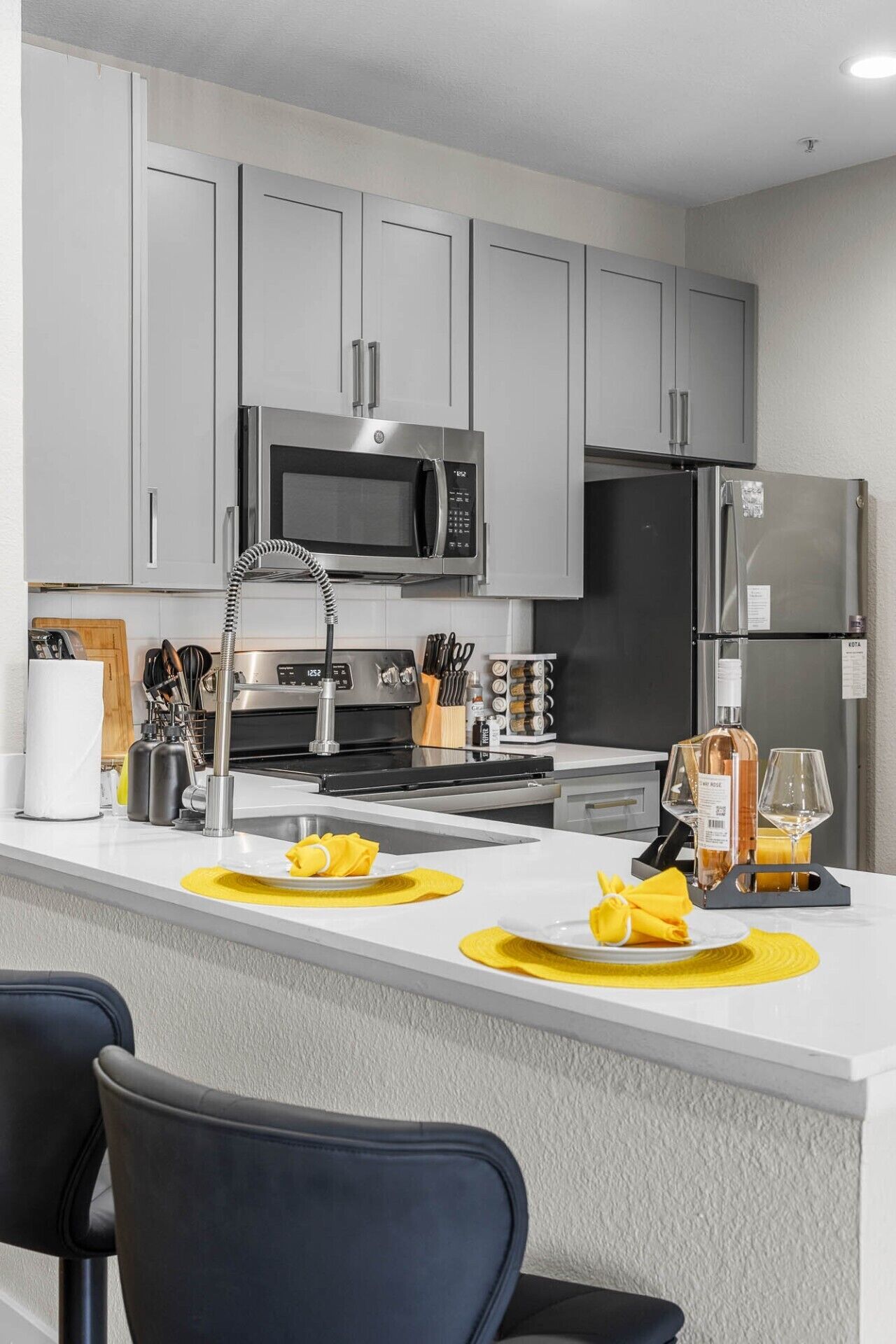 A modern kitchen with grey cabinets, a stainless steel microwave, a refrigerator, and a central island with yellow placemats.