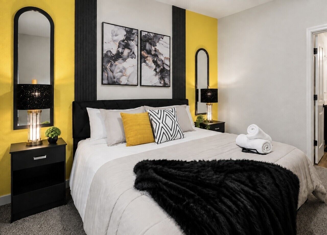 A bedroom with a bed, two bedside tables, a mirror, and artwork on the wall.