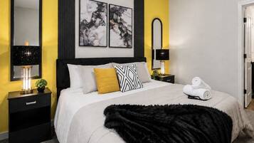 A bedroom with a bed, two bedside tables, a mirror, and artwork on the wall.