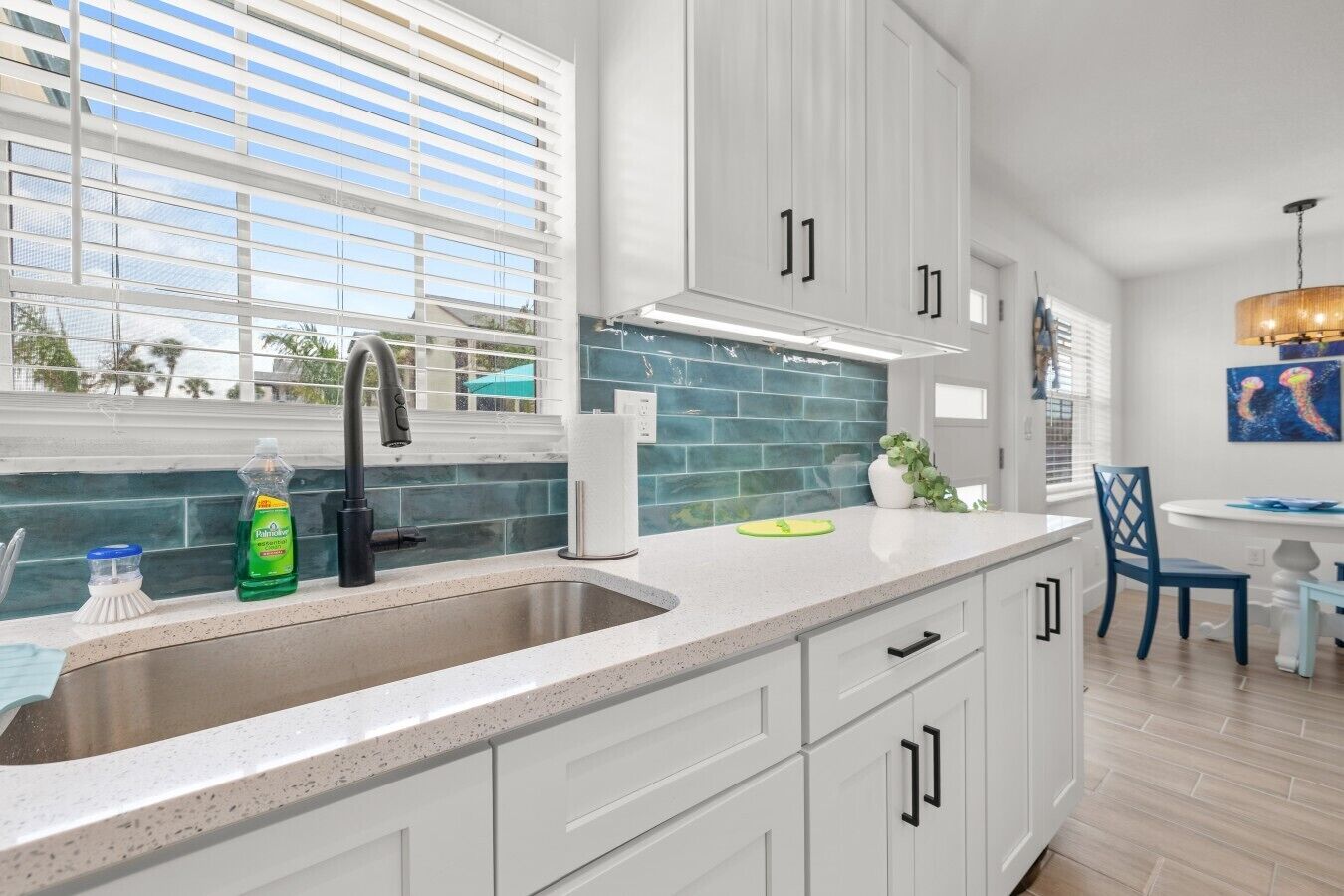 A modern kitchen with white cabinetry, a stainless steel sink, and a window with blinds.