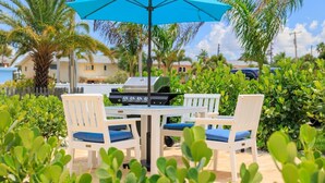 Une terrasse extérieure avec un barbecue, des chaises blanches et un parasol bleu.