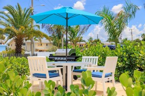 Eine Terrasse im Freien mit Grill, weißen Stühlen und einem blauen Sonnenschirm.