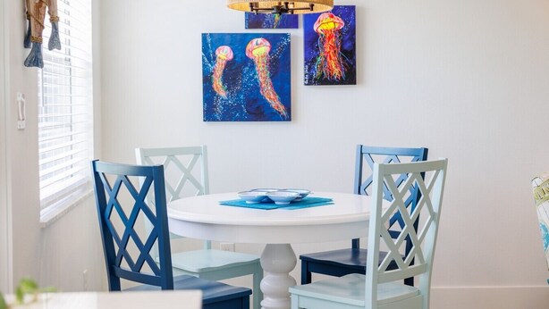 Un coin repas avec une table ronde, des chaises bleues et trois tableaux représentant des méduses, accrochés au mur.