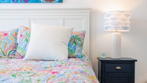 Un lit recouvert d’une couvre-lit à motifs floraux, un oreiller blanc et une table de chevet avec une lampe.