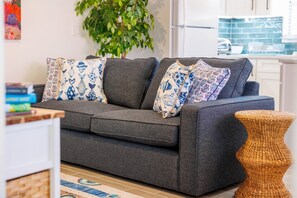 A grey sofa with patterned cushions, a woven stool, and a plant in a modern living room with a tiled floor. - Coastal Dunedin Suite Near Beaches (Dunedin)