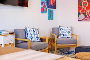 A living room with two grey armchairs, a small white side table, and a television mounted on the wall. - Coastal Dunedin Suite Near Beaches (Dunedin)