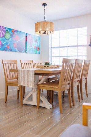 A dining area with a wooden table and chairs, a hanging light fixture, and a colorful abstract painting on the wall. - Coastal Dunedin Suite Near Beaches (Dunedin)