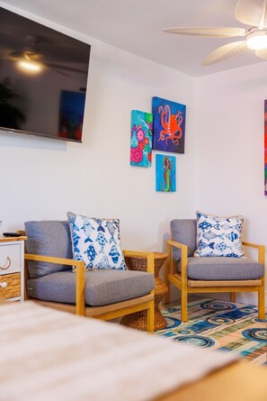 A room with two grey armchairs, a flat-screen TV mounted on the wall, and three colorful paintings. - Coastal Dunedin Suite Near Beaches (Dunedin)