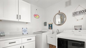 Ein Waschraum mit Waschmaschine, Trockner und Waschbecken. An der Wand befinden sich Schilder, darunter eines mit der Aufschrift 'WASH YOUR Worries AWAY'.