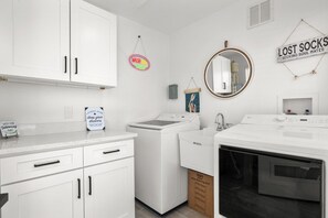 A laundry room with a washing machine, dryer, and a sink. There are signs on the wall, including one that says 'WASH YOUR Worries AWAY.' - Coastal Dunedin Suite Near Beaches (Dunedin)