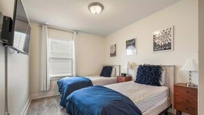 Ein Schlafzimmer mit zwei Betten, einem Fernseher, einem Fenster mit Jalousien und Wandbildern.