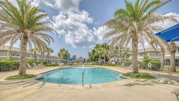 Ein Swimmingpool, umgeben von Palmen und Liegestühlen, mit blauem Himmel darüber.