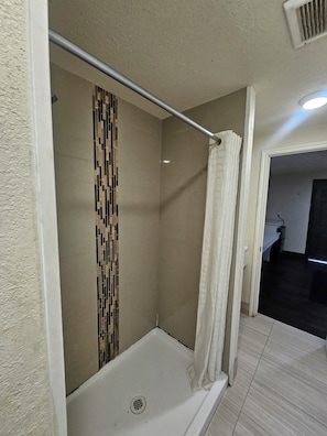 A shower area with a tiled wall, a showerhead, and a curtain.