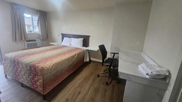 A hotel room with a bed, a desk, a chair, and a window with curtains. - Del Rancho Motel (Portland)