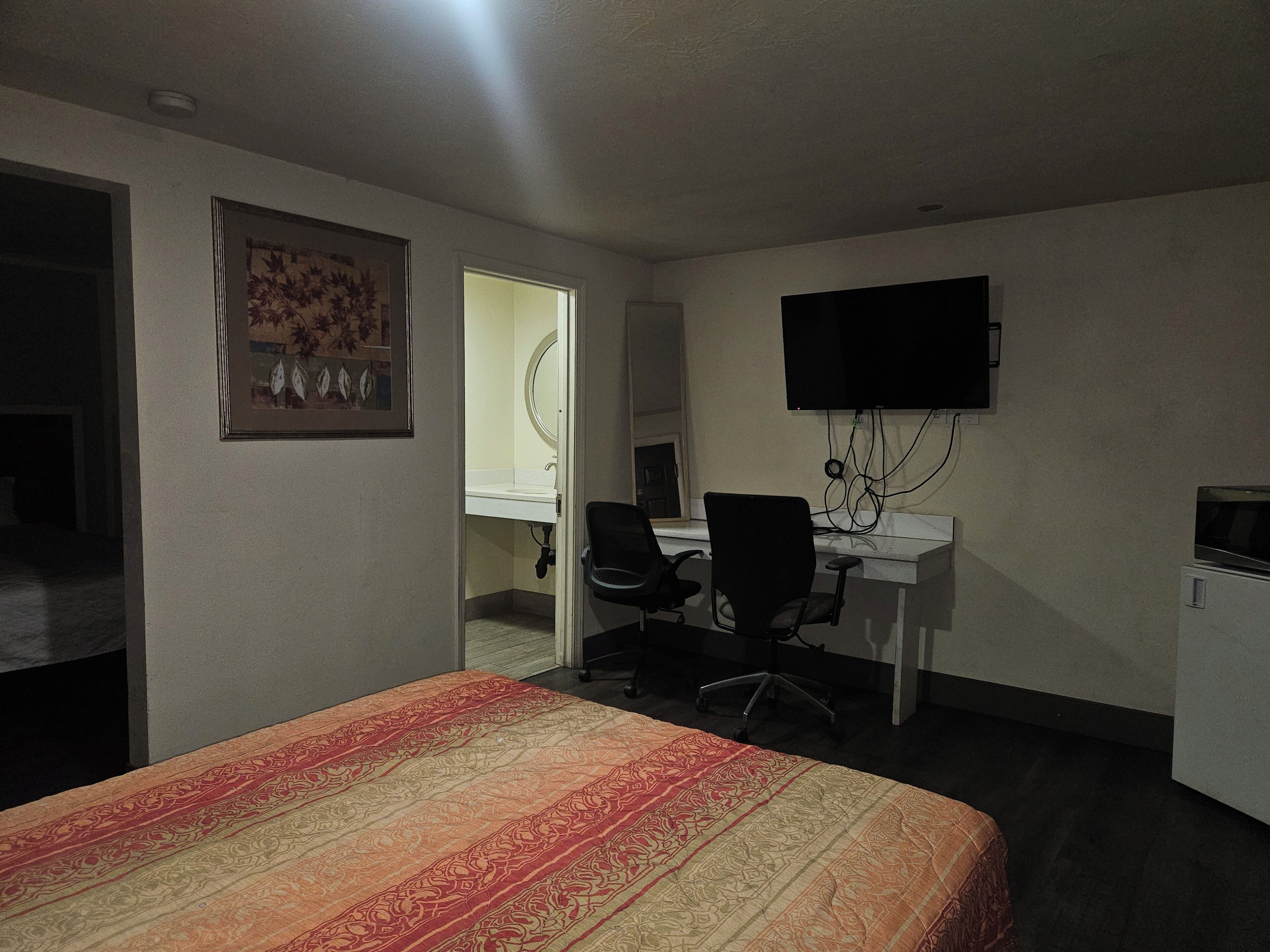 A hotel room with a bed, a desk with a chair, a television, and a bathroom visible through an open door.