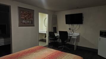 A hotel room with a bed, a desk with a chair, a television, and a bathroom visible through an open door.