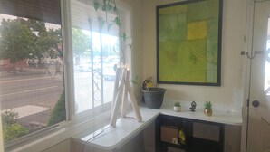 A room with a window, a wall-mounted painting, a small shelf with plants, and a door. - Del Rancho Motel (Portland)