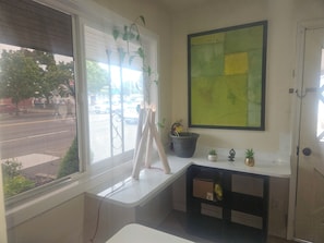 A room with a window, a wall-mounted painting, a small shelf with plants, and a door. - Del Rancho Motel (Portland)
