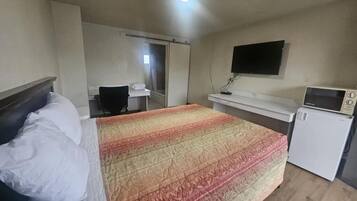 A hotel room with a bed, a desk, a television, and a microwave.