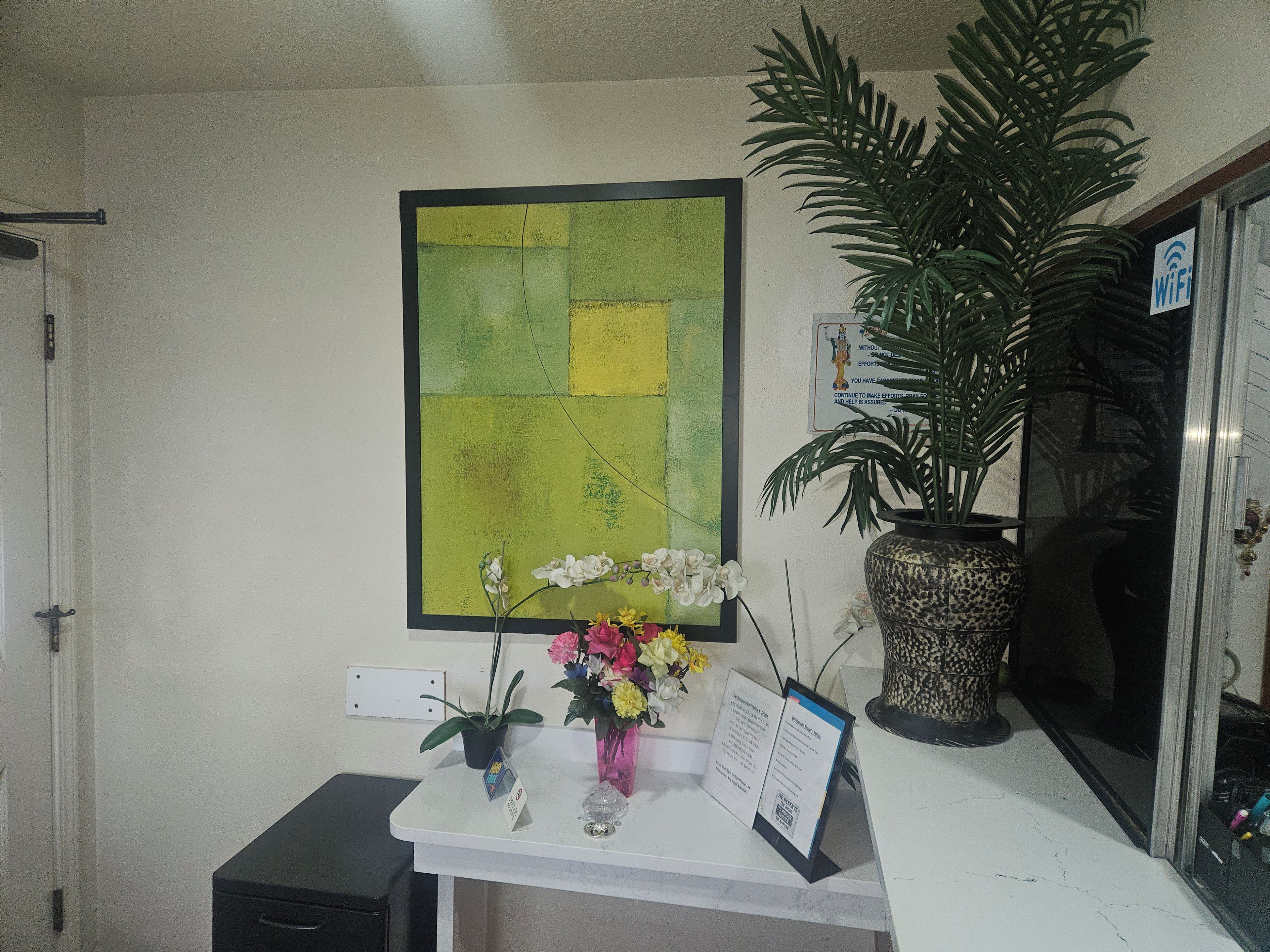 A reception desk with a framed abstract painting, a potted plant, and a sign with a WiFi symbol.