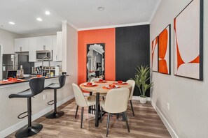 Eine moderne Küche mit weißen Schränken, ein Essbereich mit einem runden Tisch und Stühlen sowie eine Wand mit schwarzen und orangen Akzenten.