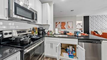 A modern kitchen with stainless steel appliances, white cabinetry, and a built-in dishwasher.