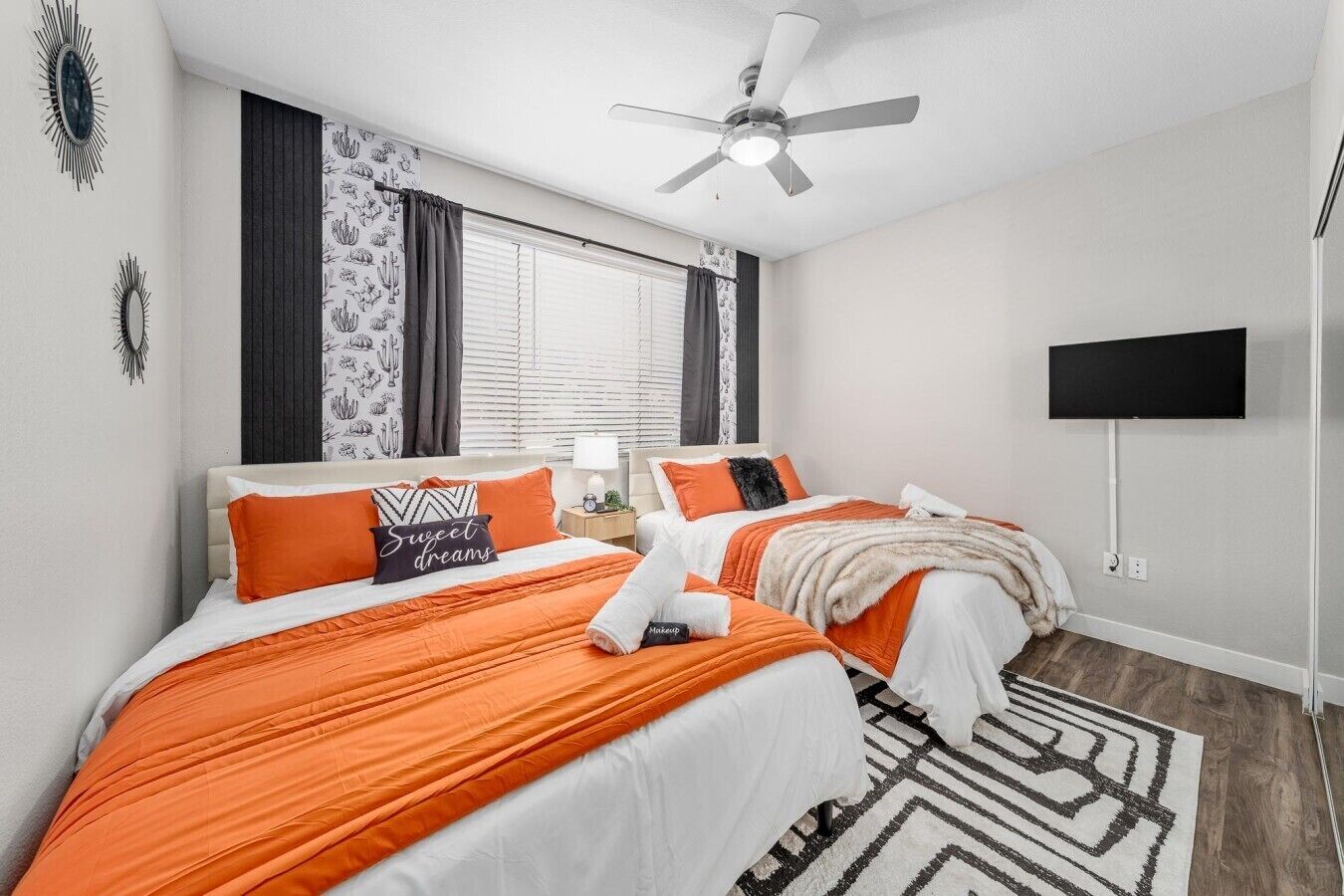 A hotel room with two beds, a ceiling fan, a flat-screen TV, and a patterned rug.