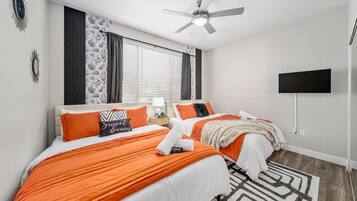 A hotel room with two beds, a ceiling fan, a flat-screen TV, and a patterned rug.