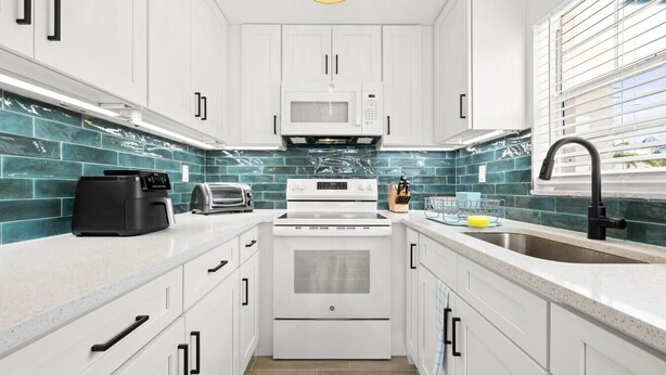 A modern kitchen with white cabinets, a microwave, a stove, a sink, and a toaster. - Colorful Coastal Retreat Near Honeymoon Island Beaches (Dunedin)
