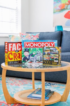 Een tafel met gezelschapsspellen, waaronder Monopoly en Fact or Crap, in een kamer met een kamerbreed tapijt en een bankstel op de achtergrond.
