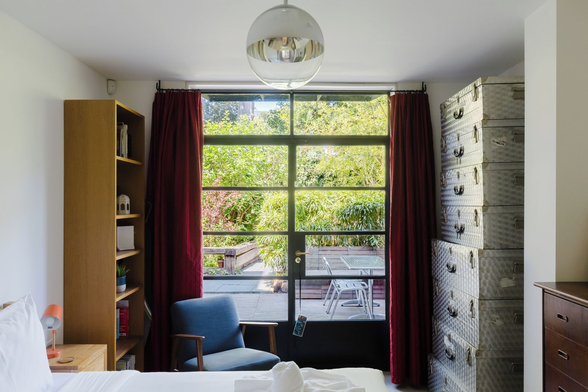 Une chambre avec une grande fenêtre, une bibliothèque, une chaise et une commode.