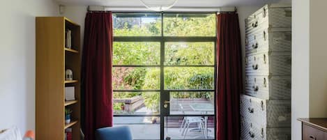 A bedroom with a large window, a bookshelf, a chair, and a dresser.