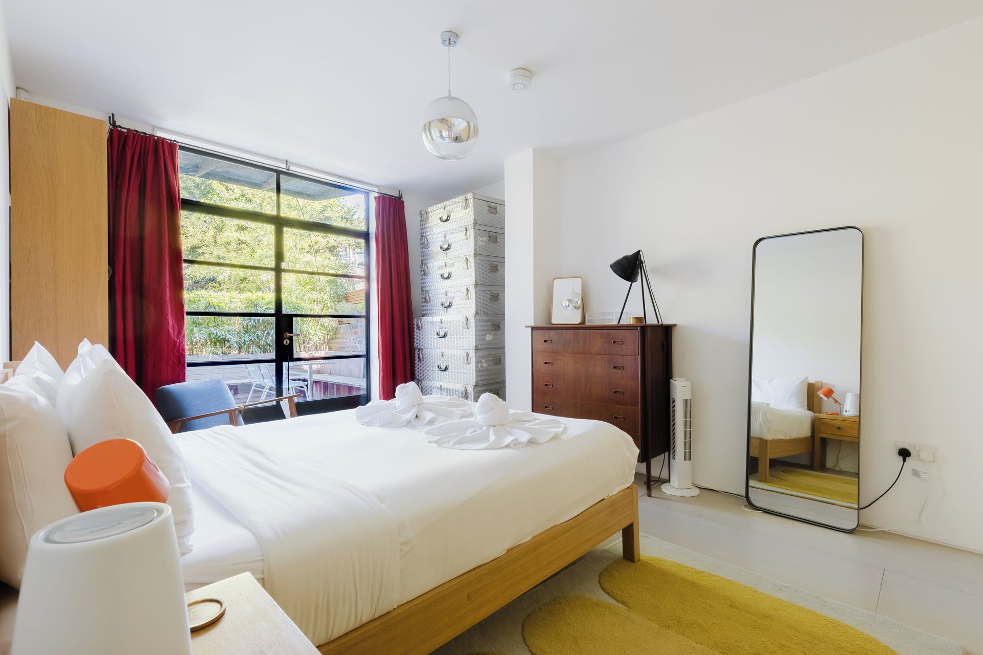 A hotel room with a bed, a wooden dresser, a mirror, and a window with curtains.