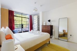 A hotel room with a bed, a wooden dresser, a mirror, and a window with curtains. - Stylish bright apartment with private garden (London)
