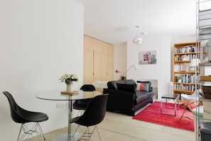 A modern living room with a glass dining table, black chairs, a black sofa, a red rug, and a bookshelf. - Stylish bright apartment with private garden (London)