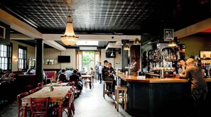 Una zona de menjador interior amb taules i cadires, una zona de bar amb un barman, i un sostre amb un disseny decoratiu.