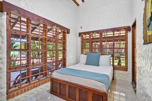 Ein Schlafzimmer mit einem Bett, Holzfensterrahmen und Blick auf Grün.