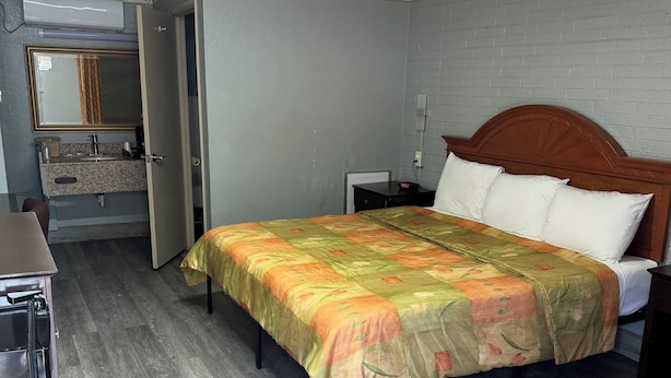 A hotel room with a bed, a nightstand, a desk, and a bathroom visible through an open door.
