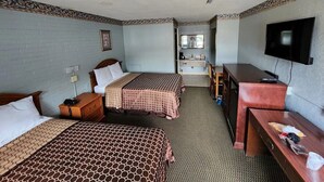 A hotel room with two beds, a desk, a television, and a bathroom visible through an open door.