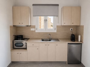 A compact kitchen with a stove, sink, and a coffee machine. - Alkinoi Residences (Sifnos)