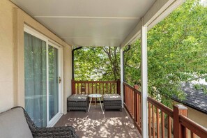 Een overdekt balkon met houten hekwerk, een glazen deur en een zithoek met een tafel en stoelen.