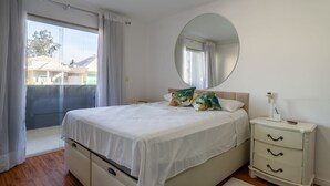Ein Schlafzimmer mit einem Bett, einem Nachttisch, einem Spiegel und einer Glastür, die auf einen Balkon führt.