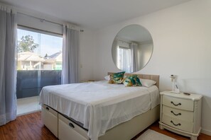 Ein Schlafzimmer mit einem Bett, einem Nachttisch, einem Spiegel und einer Glastür, die auf einen Balkon führt.
