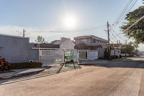 A residential street with houses, a gated entrance, and utility poles. - House with Pool in a Gated Community in Recreio (Rio de Janeiro)