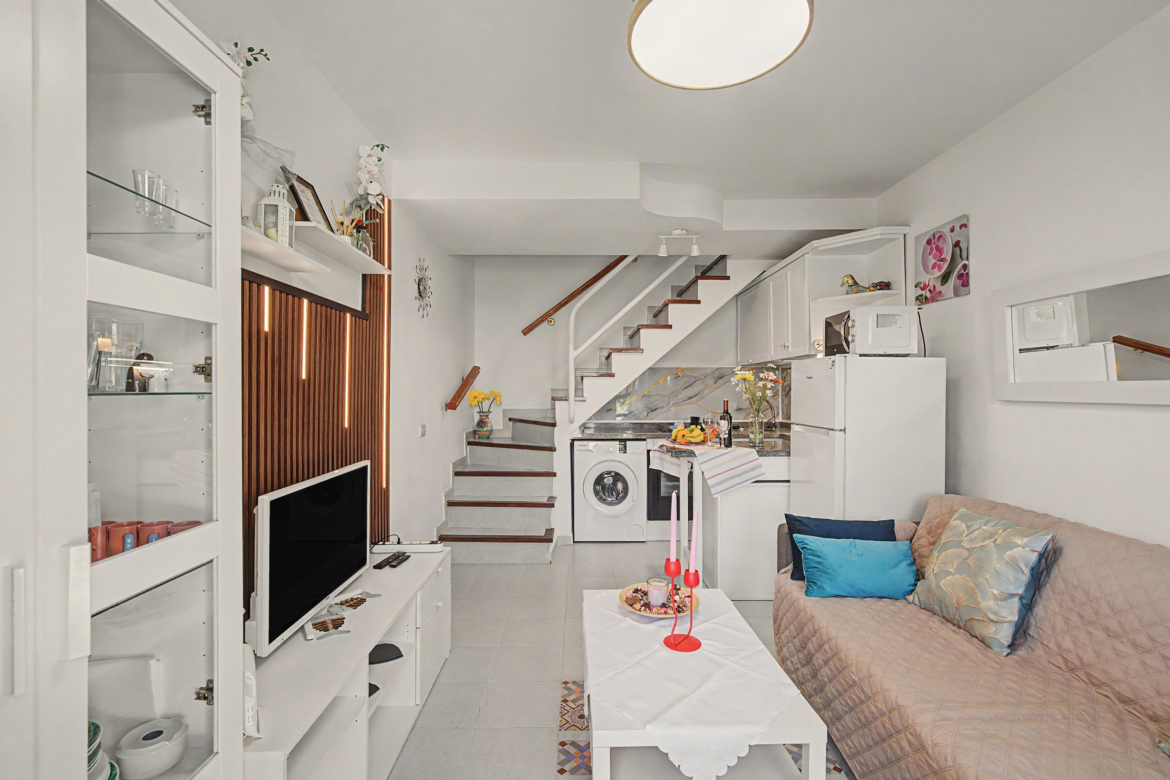 Un espace de vie compact comprenant un téléviseur, un canapé, une table à manger et un coin cuisine avec un lave-linge.
