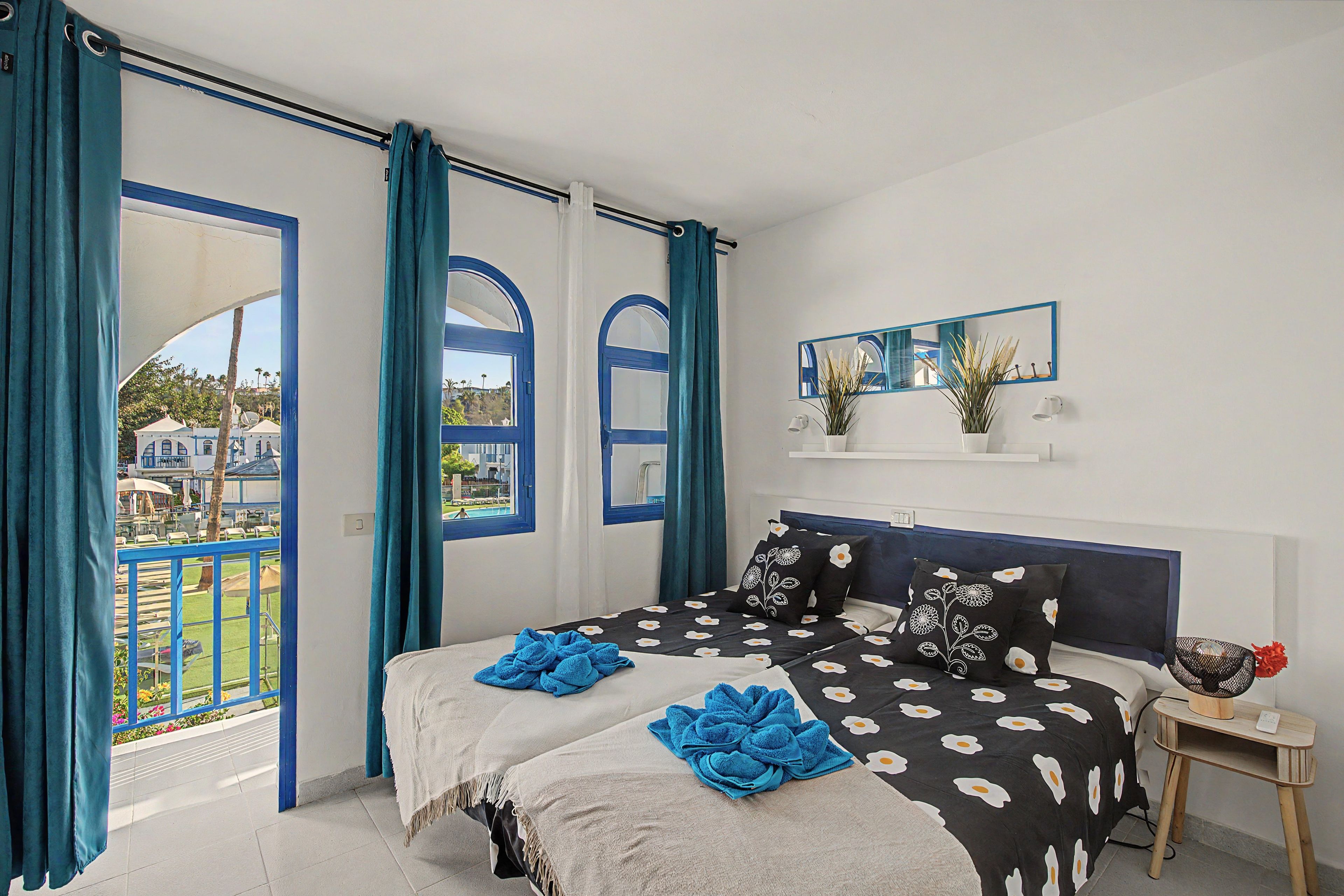 Un dormitorio con una cama, una mesita de noche, un espejo y vistas al exterior.