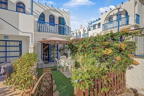 A courtyard with a table and chairs, surrounded by white buildings with blue accents and a wooden fence. -  'Casa Romantico - Playmar' with Shared Pool, Private Terrace and Wi-Fi (Maspalomas)