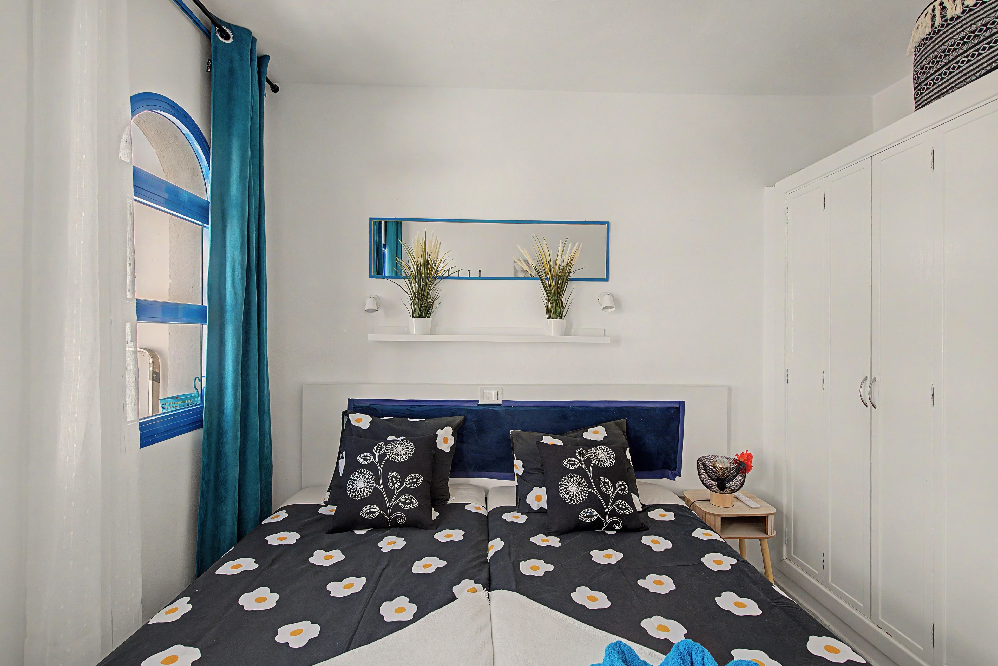 Une chambre à coucher avec un lit, un miroir, une armoire et une petite table sur laquelle est posée une plante.